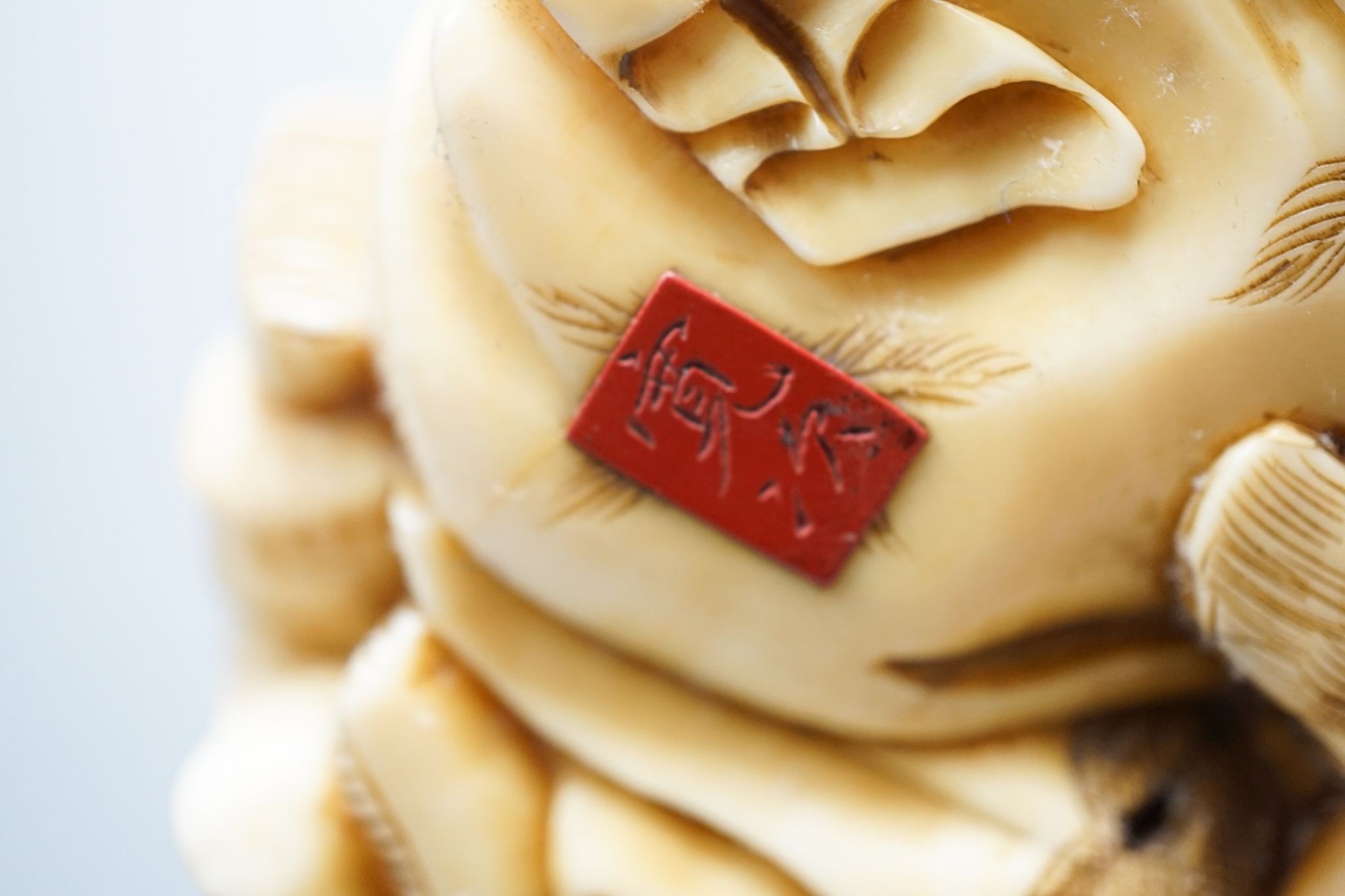 A Japanese ivory okimono of the gods Daikoku, Bishamonten and Fukurokuju, Meiji period, signed to a red lacquer tablet, 8cm wide, wood stand